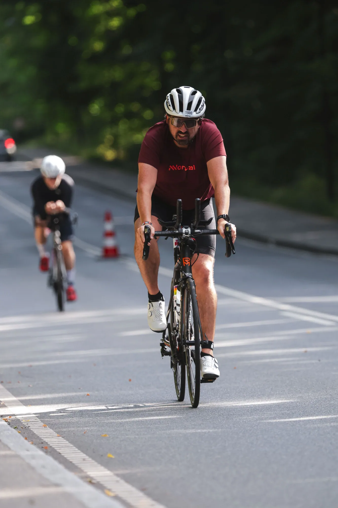 Bruno riding a black triathlon bike in a maroon kit on a tree-lined road