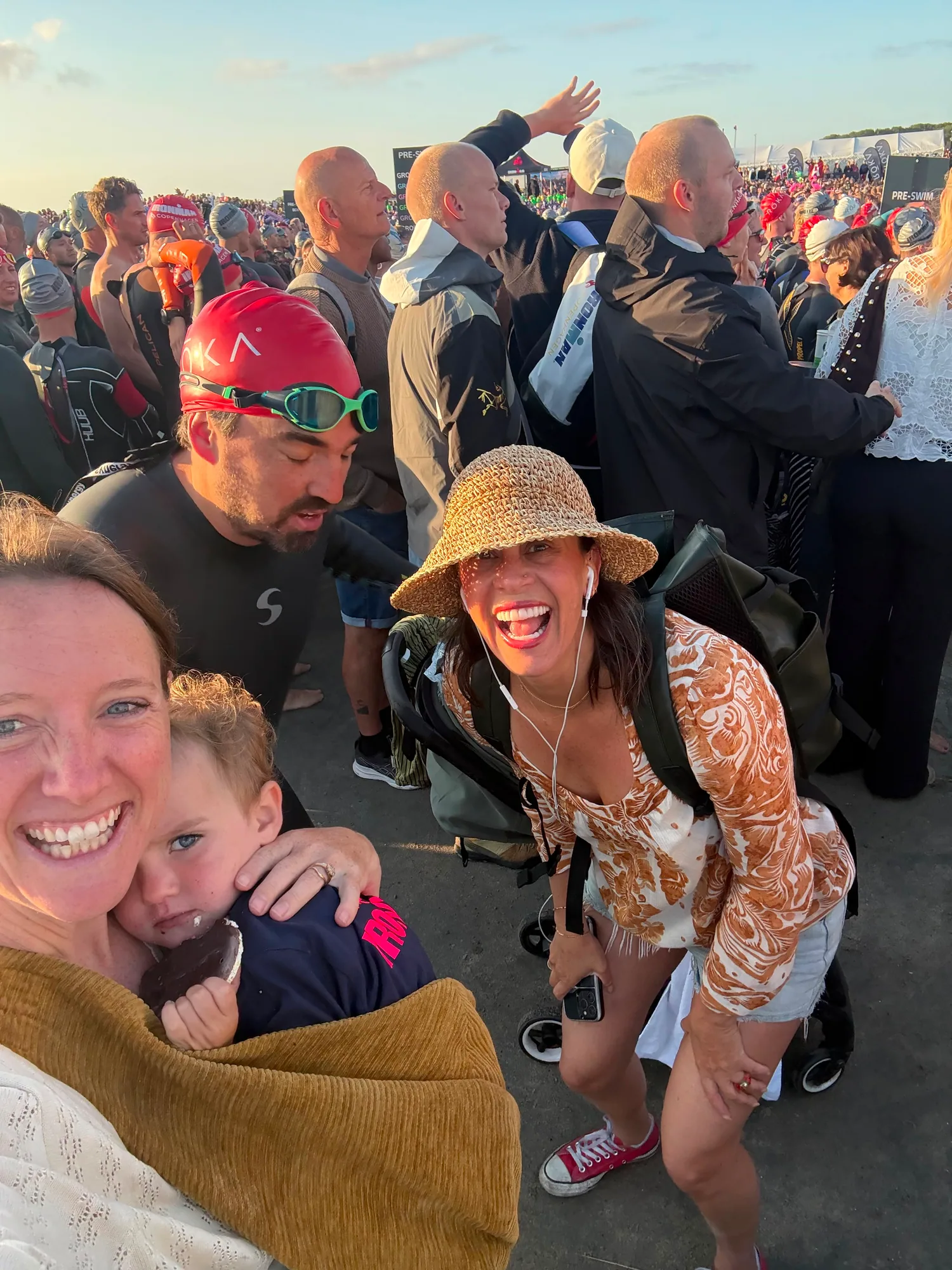 Bruno in a black wetsuit and red swim cap with smiling family and friends in the crowded swim-start area
