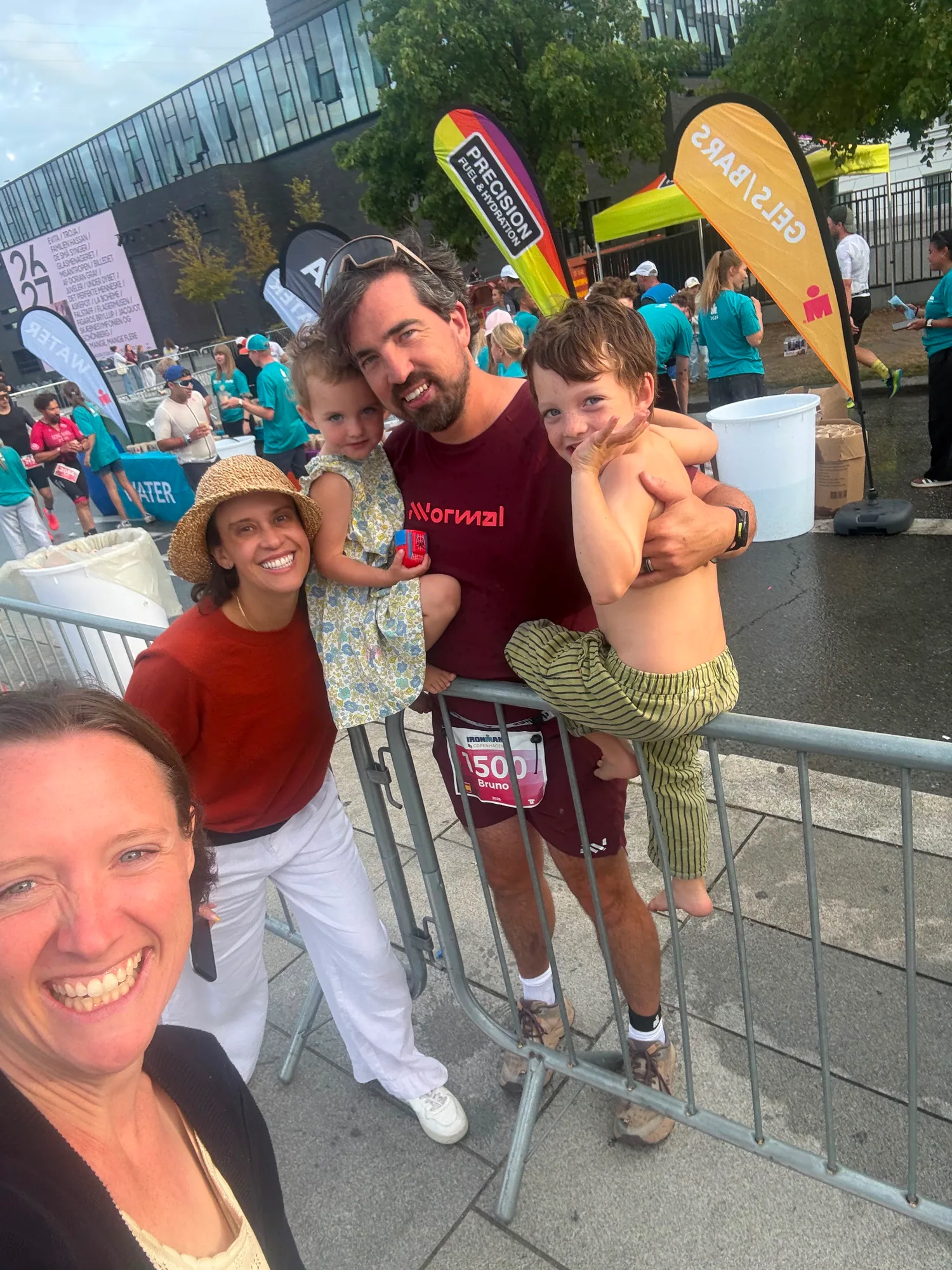 Bruno in his maroon running kit holding two children across a course barrier beside two smiling supporters